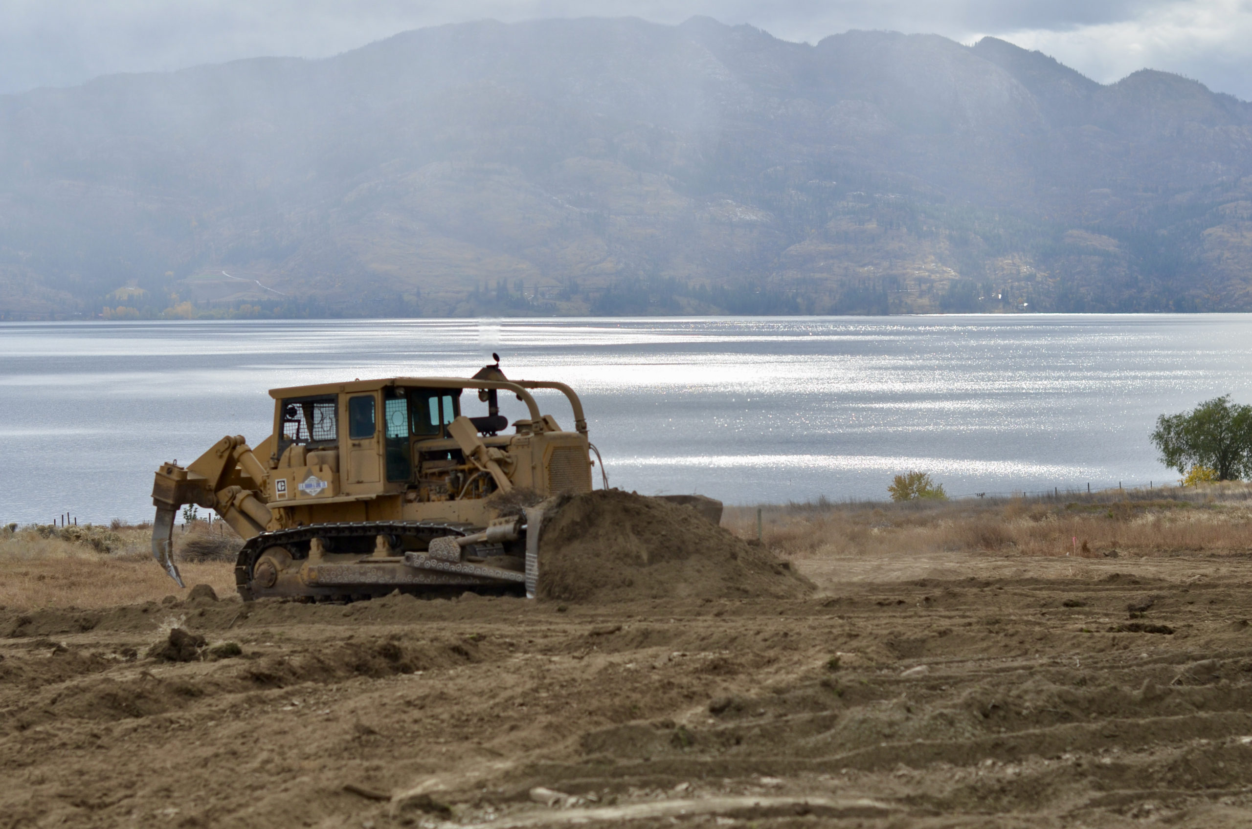 Bulldozer moves dirt around, levelling the land with a lake in the background.